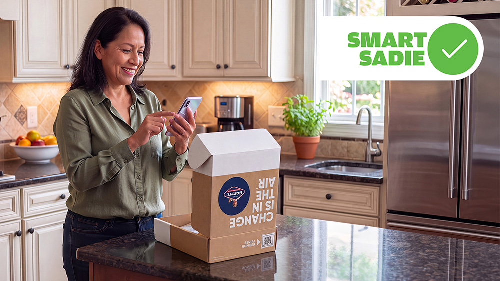 A woman stands at a kitchen island looking at her phone next to an open Goettl-branded Smart Sadie box.