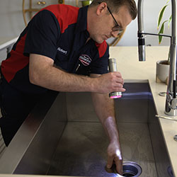 Goettl technician Robert inspecting kitchen sink drain with a flashlight.
