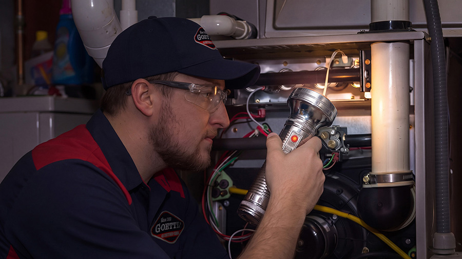 Goettl technician holding a flashlight inspecting a furnace burner